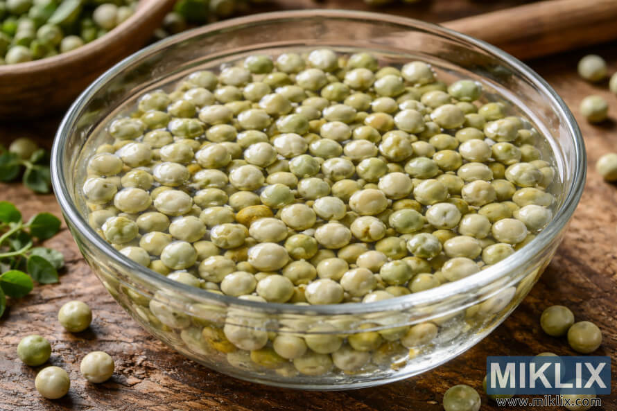 Pea seeds soaking in water in a clear glass bowl on a rustic wooden surface, prepared for planting. Pea seeds soaking in water in a clear glass bowl on a rustic wooden surface, prepared for planting.