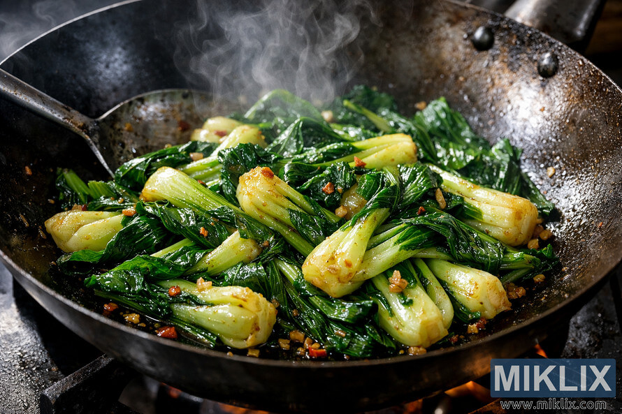 Close-up of stir-fried bok choy in a seasoned black wok with steam rising and garlic bits glistening. Close-up of stir-fried bok choy in a seasoned black wok with steam rising and garlic bits glistening.