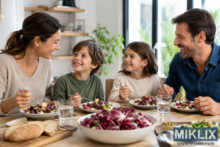A smiling family of four enjoys a healthy meal together around a wooden dining table in a bright modern home. Fresh radicchio salad, mixed greens, rustic bread, and glasses of water are arranged on the table as natural daylight streams through large windows, creating a warm atmosphere focused on healthy eating and family togetherness. A smiling family of four enjoys a healthy meal together around a wooden dining table in a bright modern home. Fresh radicchio salad, mixed greens, rustic bread, and glasses of water are arranged on the table as natural daylight streams through large windows, creating a warm atmosphere focused on healthy eating and family togetherness.