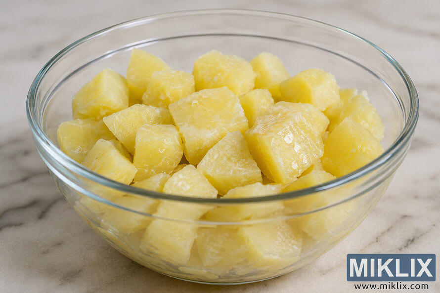 A clear glass bowl filled with cooked and cooled potato chunks on a light marble countertop, photographed in soft natural light to illustrate resistant starch formation after cooling. A clear glass bowl filled with cooked and cooled potato chunks on a light marble countertop, photographed in soft natural light to illustrate resistant starch formation after cooling.
