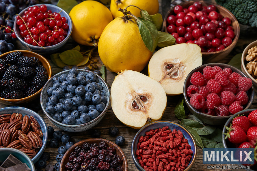 Top-down landscape photo of antioxidant-rich foods including whole and sliced quince, blueberries, raspberries, blackberries, strawberries, red currants, cranberries, nuts, and dried berries arranged in ceramic bowls on a rustic wooden table with soft natural lighting. Top-down landscape photo of antioxidant-rich foods including whole and sliced quince, blueberries, raspberries, blackberries, strawberries, red currants, cranberries, nuts, and dried berries arranged in ceramic bowls on a rustic wooden table with soft natural lighting.
