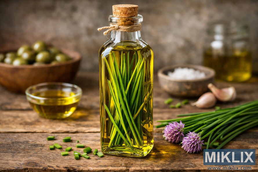 A tall glass bottle of chive-infused olive oil stands on a rustic wooden table, filled with golden-yellow oil and long green chive stalks. A tall glass bottle of chive-infused olive oil stands on a rustic wooden table, filled with golden-yellow oil and long green chive stalks.