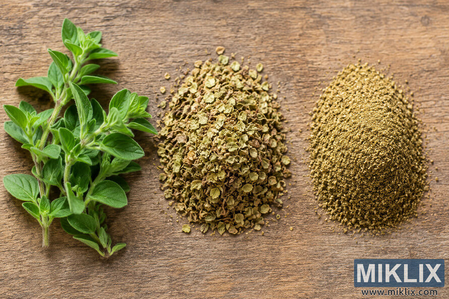 Fresh oregano sprigs, dried oregano flakes, and finely ground oregano powder arranged side by side on a rustic wooden tabletop in a high-resolution landscape composition. Fresh oregano sprigs, dried oregano flakes, and finely ground oregano powder arranged side by side on a rustic wooden tabletop in a high-resolution landscape composition.