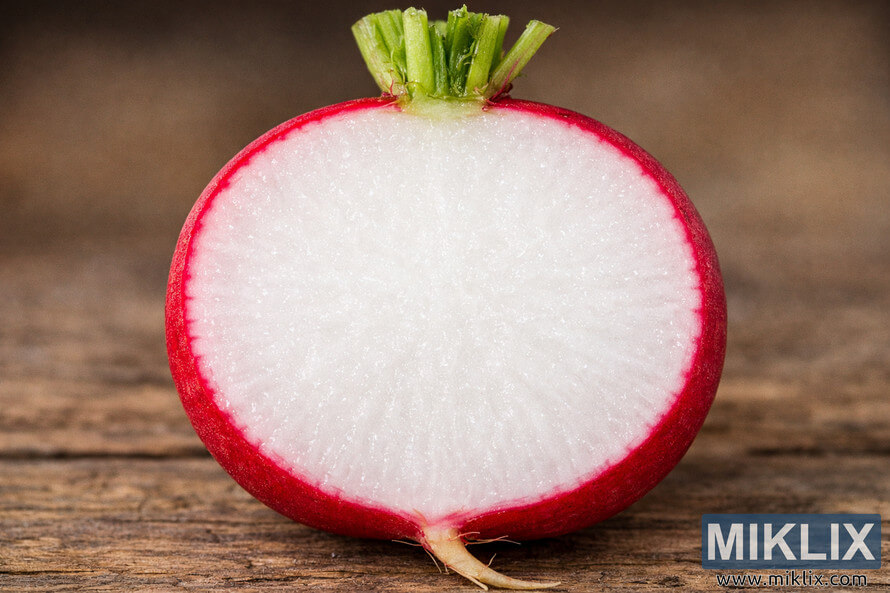 Close-up cross-section of a freshly cut radish revealing a crisp white interior surrounded by vibrant red skin on a rustic wooden surface