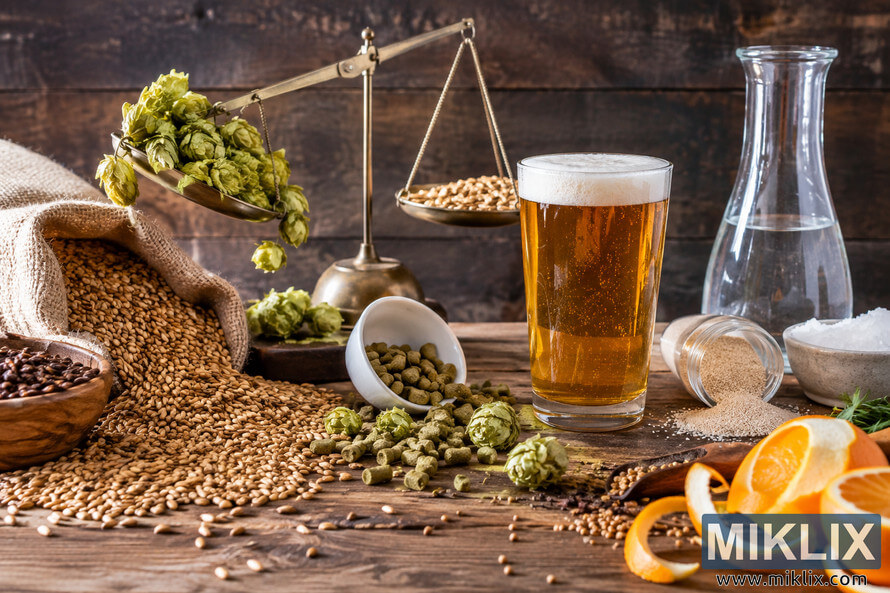 Rustic still life of an amber beer beside a tilted brass balance scale overloaded with hops, surrounded by spilled malt grains, hop pellets, yeast, water, citrus peel, spices, and brewing ingredients. Rustic still life of an amber beer beside a tilted brass balance scale overloaded with hops, surrounded by spilled malt grains, hop pellets, yeast, water, citrus peel, spices, and brewing ingredients.