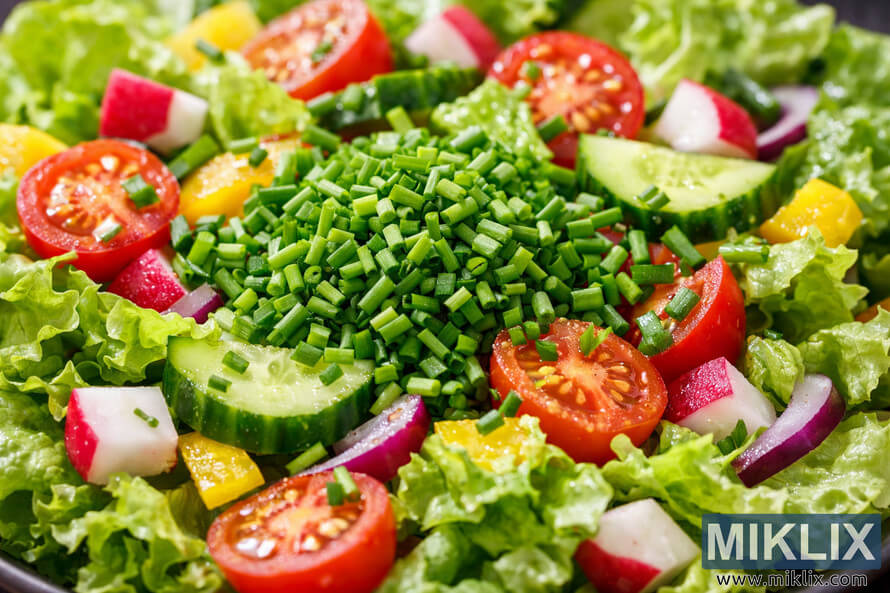 Close-up of a fresh vegetable salad topped with finely chopped chives, surrounded by lettuce, tomatoes, cucumbers, bell peppers, radishes, and onions. Close-up of a fresh vegetable salad topped with finely chopped chives, surrounded by lettuce, tomatoes, cucumbers, bell peppers, radishes, and onions.
