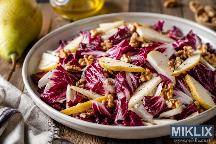 A vibrant radicchio salad with crisp pear slices and walnuts served in a light ceramic bowl on a rustic wooden table, surrounded by soft natural light, a linen napkin, and simple kitchen elements. A vibrant radicchio salad with crisp pear slices and walnuts served in a light ceramic bowl on a rustic wooden table, surrounded by soft natural light, a linen napkin, and simple kitchen elements.