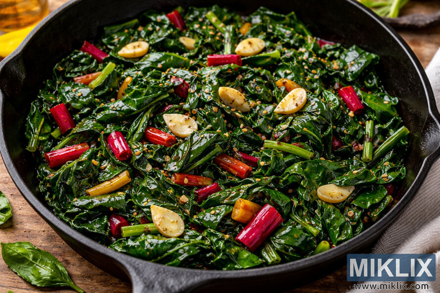 SautÃ©ed Swiss chard with colorful stems and sliced garlic glistening in olive oil in a cast iron skillet.