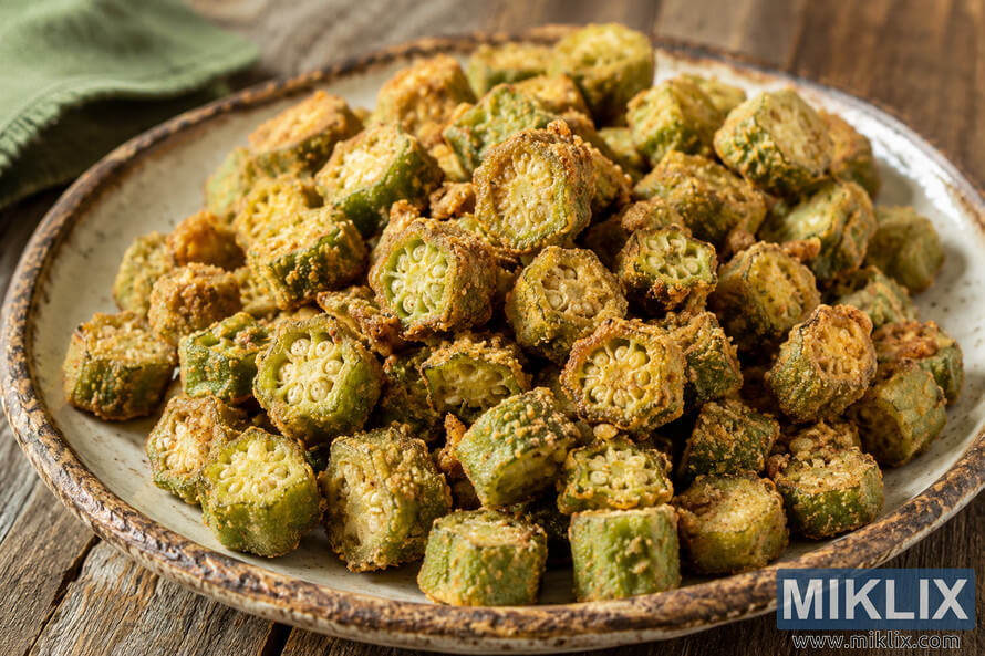 Close-up landscape photograph of crispy southern fried okra served on a rustic ceramic plate atop a weathered wooden table, with golden crunchy coating, visible green okra centers, warm natural lighting, shallow depth of field, and a softly blurred green cloth in the background. Close-up landscape photograph of crispy southern fried okra served on a rustic ceramic plate atop a weathered wooden table, with golden crunchy coating, visible green okra centers, warm natural lighting, shallow depth of field, and a softly blurred green cloth in the background.