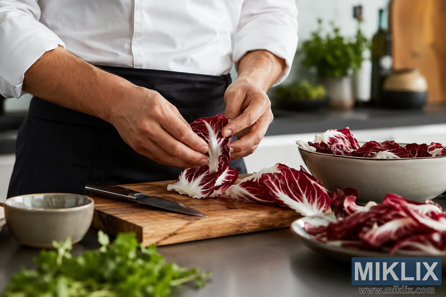 Close-up landscape image of a chefâs hands preparing fresh radicchio on a wooden cutting board in a bright modern kitchen, with ceramic bowls, a kitchen knife, and softly blurred herbs in the background. Close-up landscape image of a chefâs hands preparing fresh radicchio on a wooden cutting board in a bright modern kitchen, with ceramic bowls, a kitchen knife, and softly blurred herbs in the background.