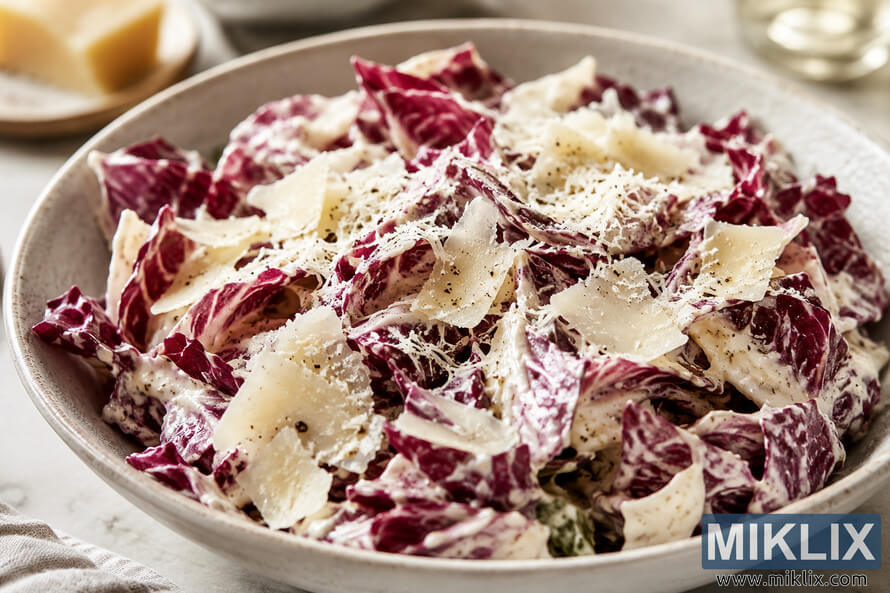 A creamy Caesar-style radicchio salad served in a rustic ceramic bowl, generously topped with shaved and grated parmesan, cracked black pepper, and rich dressing on a light marble surface with a softly blurred background. A creamy Caesar-style radicchio salad served in a rustic ceramic bowl, generously topped with shaved and grated parmesan, cracked black pepper, and rich dressing on a light marble surface with a softly blurred background.