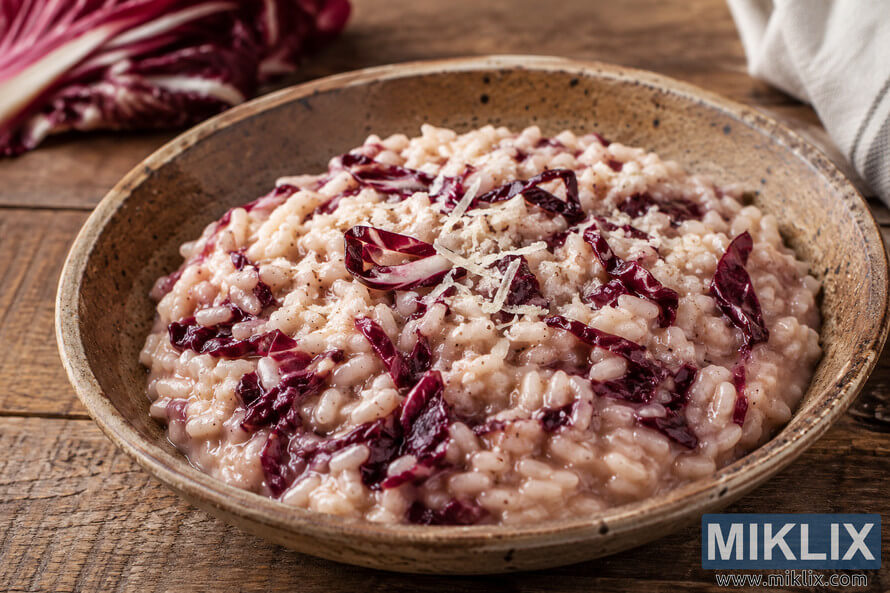 A creamy traditional Italian risotto with deep burgundy radicchio pieces served in a rustic ceramic bowl on a weathered wooden table, illuminated by warm natural light with fresh radicchio in the softly blurred background. A creamy traditional Italian risotto with deep burgundy radicchio pieces served in a rustic ceramic bowl on a weathered wooden table, illuminated by warm natural light with fresh radicchio in the softly blurred background.