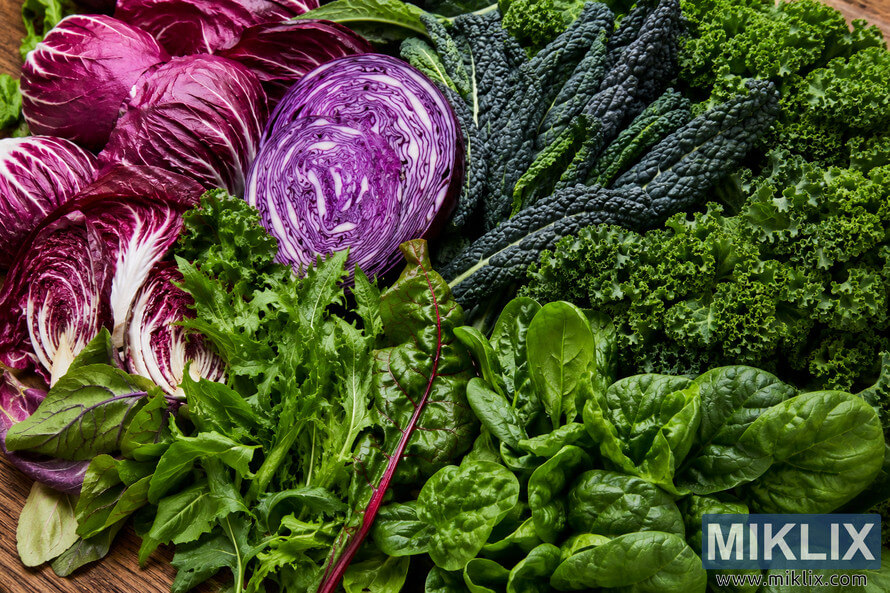 A vibrant assortment of fresh leafy greens, including radicchio, kale, spinach, and red cabbage, arranged closely together on a rustic wooden surface with rich natural colors and detailed textures. A vibrant assortment of fresh leafy greens, including radicchio, kale, spinach, and red cabbage, arranged closely together on a rustic wooden surface with rich natural colors and detailed textures.