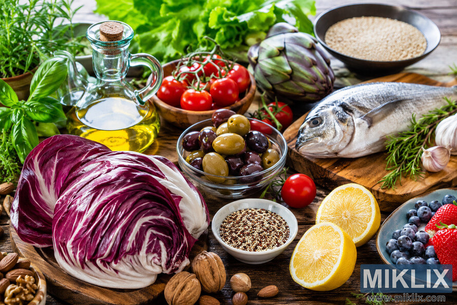 High-resolution landscape food photograph featuring fresh Mediterranean diet ingredients arranged on a rustic wooden table, including radicchio, olive oil, tomatoes, olives, whole grains, fish, herbs, garlic, lemons, berries, nuts, leafy greens, and an artichoke in natural daylight. High-resolution landscape food photograph featuring fresh Mediterranean diet ingredients arranged on a rustic wooden table, including radicchio, olive oil, tomatoes, olives, whole grains, fish, herbs, garlic, lemons, berries, nuts, leafy greens, and an artichoke in natural daylight.