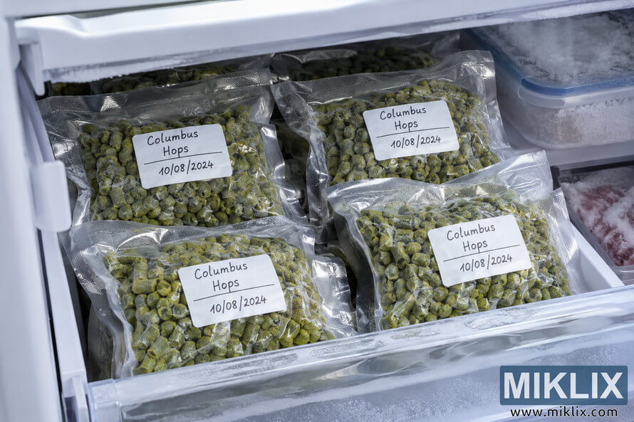 Landscape view inside a frosty freezer drawer containing several vacuum-sealed bags of green Columbus hop pellets, neatly labeled with the hop variety and storage date. Landscape view inside a frosty freezer drawer containing several vacuum-sealed bags of green Columbus hop pellets, neatly labeled with the hop variety and storage date.