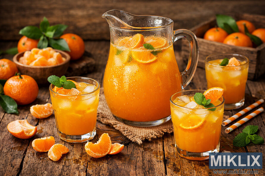 Pitcher and glasses of fresh tangerine juice with ice, mint, and tangerine slices on a rustic wooden table
