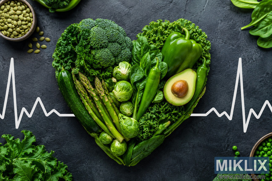 Heart-shaped arrangement of fresh green vegetables including broccoli, kale, avocado, asparagus, spinach, Brussels sprouts, and peppers on a dark textured background with a white heartbeat line symbolizing cardiovascular health and healthy eating. Heart-shaped arrangement of fresh green vegetables including broccoli, kale, avocado, asparagus, spinach, Brussels sprouts, and peppers on a dark textured background with a white heartbeat line symbolizing cardiovascular health and healthy eating.