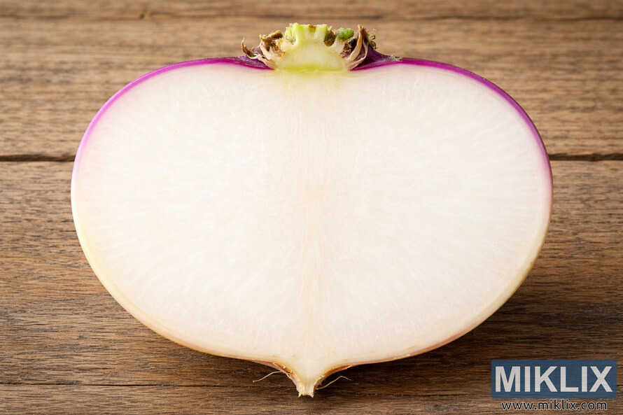 High-resolution cross-section of a purple-top white globe turnip showing smooth white interior flesh and purple skin on a rustic wooden surface.