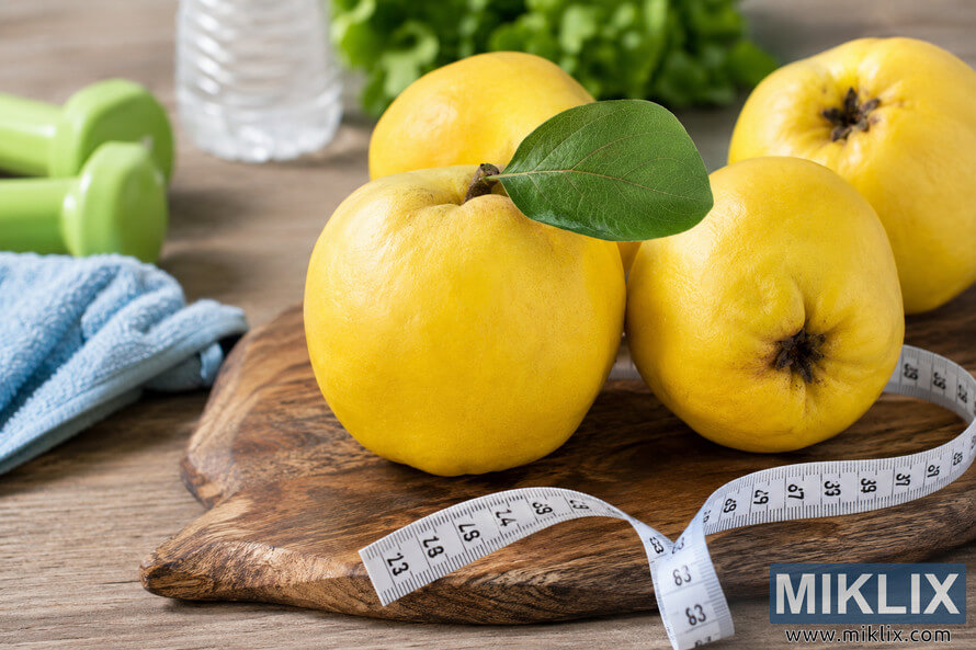 Fresh yellow quince fruits arranged on a rustic wooden cutting board with a measuring tape, towel, dumbbells, water bottle, and green salad in the background, symbolizing healthy nutrition, fitness, wellness, and balanced lifestyle habits. Fresh yellow quince fruits arranged on a rustic wooden cutting board with a measuring tape, towel, dumbbells, water bottle, and green salad in the background, symbolizing healthy nutrition, fitness, wellness, and balanced lifestyle habits.