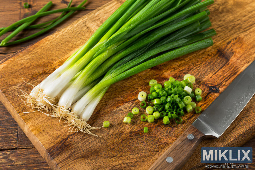 Fresh green onions and scallions arranged on a rustic wooden cutting board beside a chefâs knife, with chopped scallion slices scattered across the surface in warm natural lighting. Fresh green onions and scallions arranged on a rustic wooden cutting board beside a chefâs knife, with chopped scallion slices scattered across the surface in warm natural lighting.