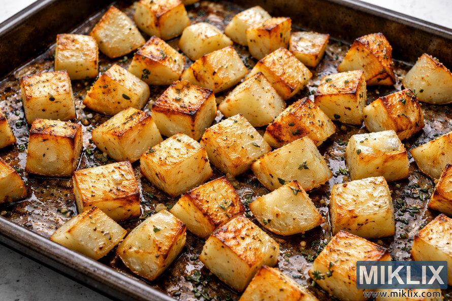 Roasted turnip cubes with golden brown edges arranged on a seasoned baking sheet