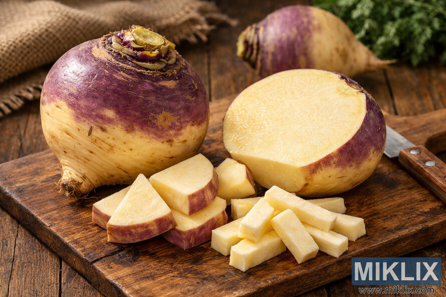 Fresh rutabaga root vegetable with purple crown and cream-colored flesh resting on a rustic wooden cutting board.
