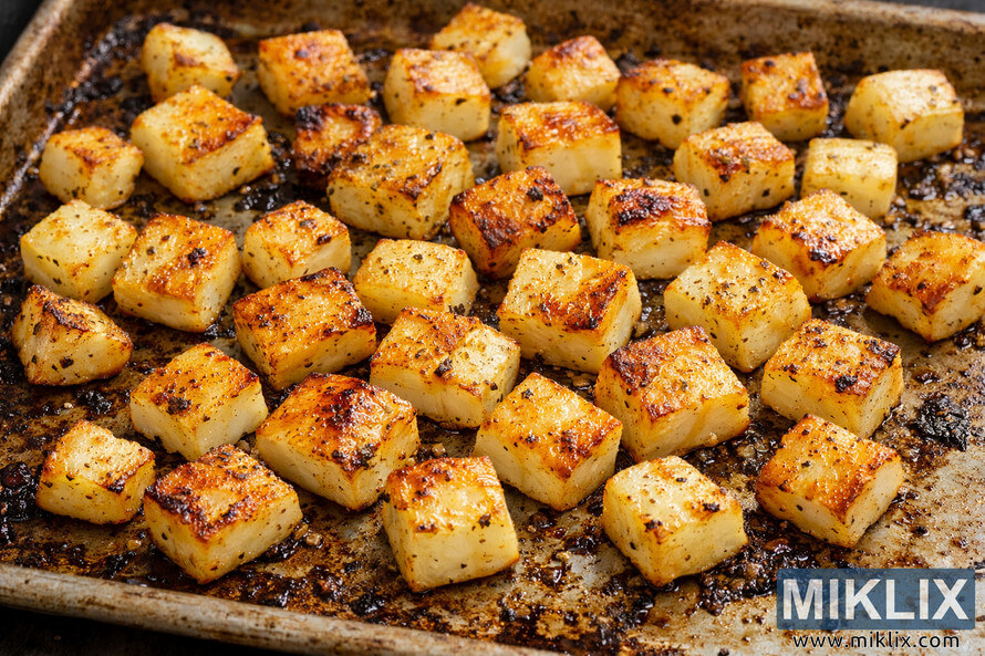 Close-up photo of golden roasted turnip cubes scattered across a rustic, well-used baking sheet, with crisp, caramelized edges, visible black pepper and green herb seasoning, and a warm, natural light that highlights the glistening oil and rich golden-brown color of the vegetables. Close-up photo of golden roasted turnip cubes scattered across a rustic, well-used baking sheet, with crisp, caramelized edges, visible black pepper and green herb seasoning, and a warm, natural light that highlights the glistening oil and rich golden-brown color of the vegetables.