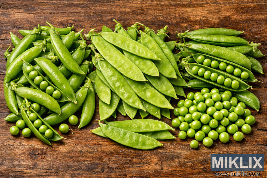 High-resolution photo showing snap peas, snow peas, and shelling peas arranged side by side on a rustic wooden surface High-resolution photo showing snap peas, snow peas, and shelling peas arranged side by side on a rustic wooden surface