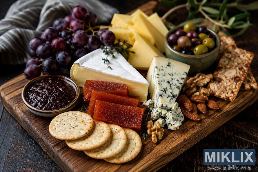 A beautifully arranged rustic cheese board displayed on a dark wooden table, featuring creamy brie, blue cheese, quince paste, red grapes, mixed olives, artisan crackers, almonds, walnuts, and fig spread in warm natural lighting. A beautifully arranged rustic cheese board displayed on a dark wooden table, featuring creamy brie, blue cheese, quince paste, red grapes, mixed olives, artisan crackers, almonds, walnuts, and fig spread in warm natural lighting.