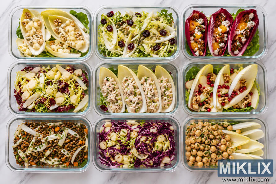 Top-down view of nine glass meal prep containers arranged on a marble surface, each filled with colorful endive-based salads featuring fruits, nuts, grains, legumes, cheeses, and fresh greens in a clean weekly food prep layout. Top-down view of nine glass meal prep containers arranged on a marble surface, each filled with colorful endive-based salads featuring fruits, nuts, grains, legumes, cheeses, and fresh greens in a clean weekly food prep layout.