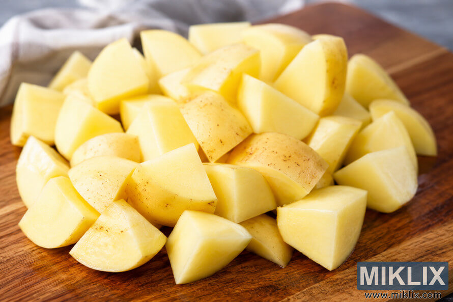 High-resolution landscape photo of freshly pre-cut potato chunks arranged on a wooden cutting board, ready for quick cooking, with a softly blurred kitchen background. High-resolution landscape photo of freshly pre-cut potato chunks arranged on a wooden cutting board, ready for quick cooking, with a softly blurred kitchen background.