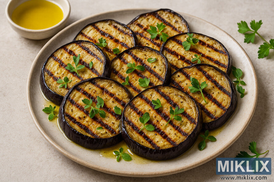 Yankakken eggplant da aka gasa a kan farantin yumbu da aka Æawata da sabbin ganye da man zaitun