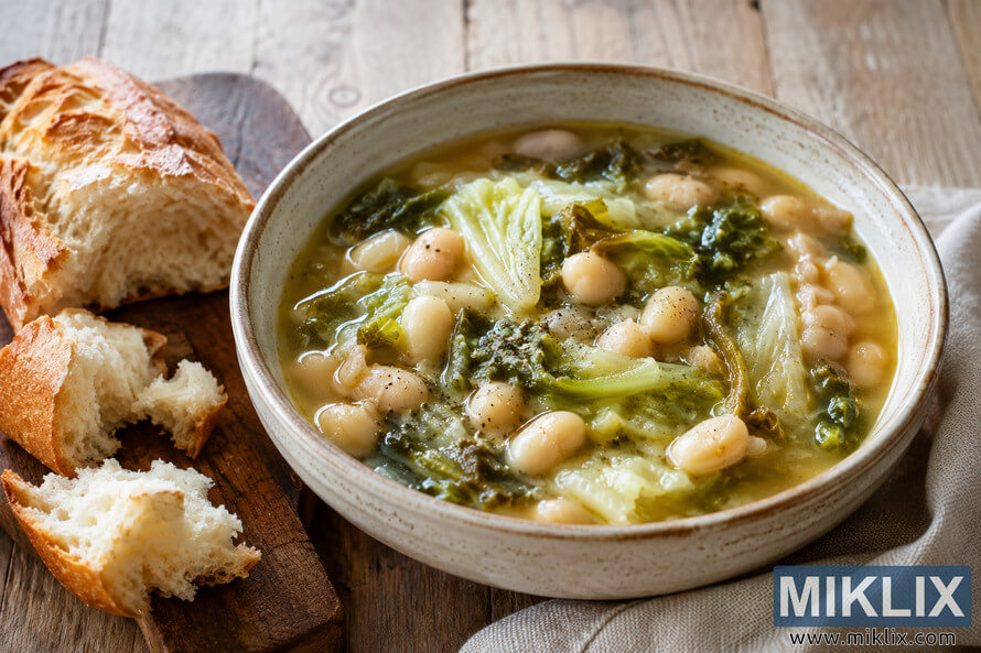 A rustic ceramic bowl filled with white bean soup and escarole sits on a weathered wooden table beside torn pieces of crusty bread on a wooden cutting board, illuminated by soft natural light. A rustic ceramic bowl filled with white bean soup and escarole sits on a weathered wooden table beside torn pieces of crusty bread on a wooden cutting board, illuminated by soft natural light.