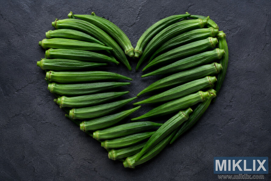 A high-resolution landscape image showing fresh green okra pods carefully arranged into a symmetrical heart shape on a dark textured background, symbolizing cardiovascular health, wellness, healthy eating, and natural nutrition. A high-resolution landscape image showing fresh green okra pods carefully arranged into a symmetrical heart shape on a dark textured background, symbolizing cardiovascular health, wellness, healthy eating, and natural nutrition.