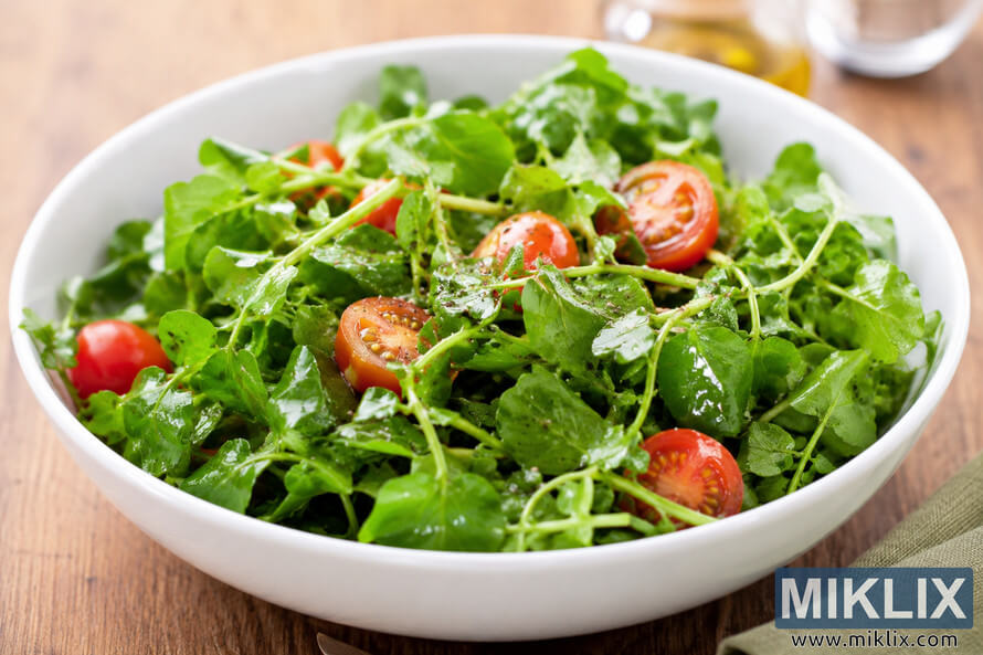 Fresh watercress salad served in a white ceramic bowl with halved cherry tomatoes and light vinaigrette dressing on a rustic wooden table. Fresh watercress salad served in a white ceramic bowl with halved cherry tomatoes and light vinaigrette dressing on a rustic wooden table.