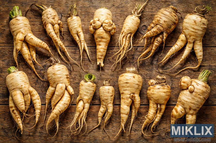 Various misshapen parsnip roots with forked, twisted, and bulbous growth patterns arranged on a rustic wooden surface.