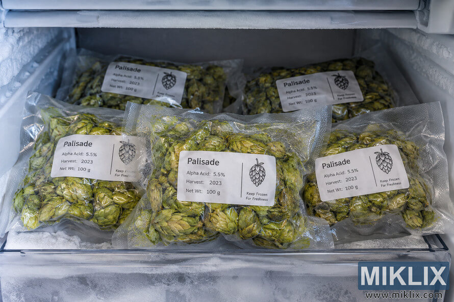 Several vacuum-sealed packages of green Palisade hops with generic white labels stacked inside a frost-covered freezer compartment. Several vacuum-sealed packages of green Palisade hops with generic white labels stacked inside a frost-covered freezer compartment.