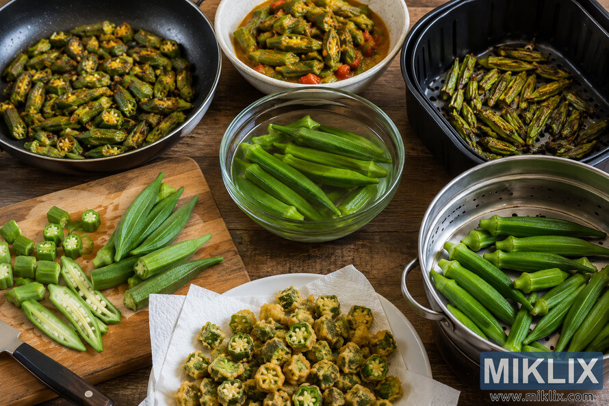 Landscape photograph showing multiple okra preparation techniques on a rustic wooden table, including fresh sliced okra on a cutting board, whole okra soaking in water, sautéed okra in a frying pan, stewed okra with tomatoes in a bowl, roasted okra in an air-fryer-style basket, steamed whole okra in a metal steamer, and crispy fried okra on a paper-lined plate. Landscape photograph showing multiple okra preparation techniques on a rustic wooden table, including fresh sliced okra on a cutting board, whole okra soaking in water, sautéed okra in a frying pan, stewed okra with tomatoes in a bowl, roasted okra in an air-fryer-style basket, steamed whole okra in a metal steamer, and crispy fried okra on a paper-lined plate.